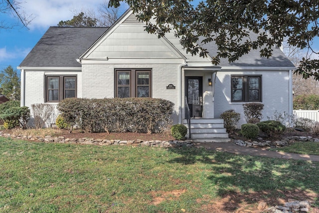 view of front facade featuring a front yard, brick siding, and roof with shingles