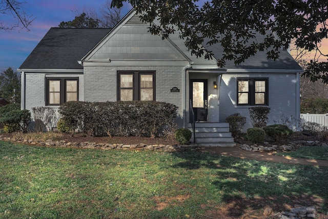 bungalow-style home with brick siding, a shingled roof, and a front lawn