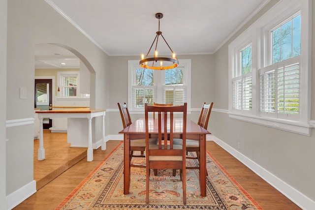 dining space featuring arched walkways, a chandelier, ornamental molding, and light wood finished floors