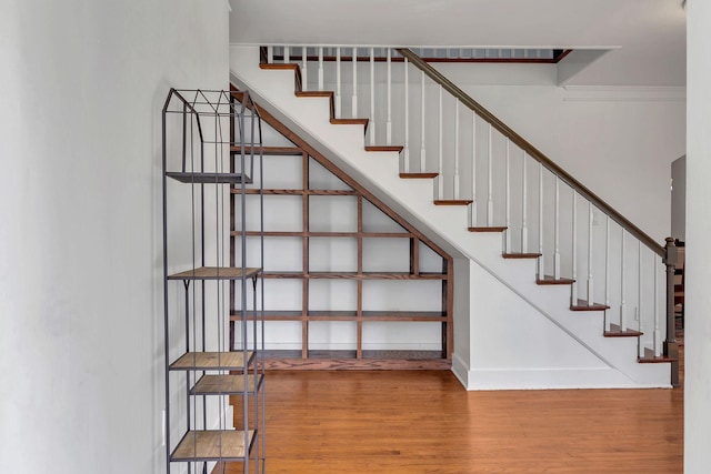 stairway with wood finished floors, baseboards, and ornamental molding