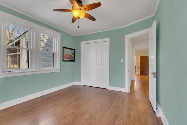 unfurnished bedroom featuring wood finished floors, baseboards, ceiling fan, a closet, and crown molding