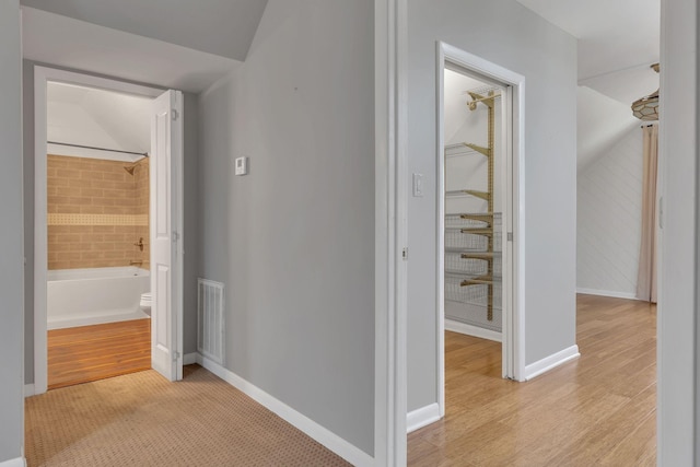 hallway with visible vents, baseboards, and light wood finished floors