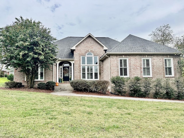 view of front of property with brick siding, a front yard, and roof with shingles