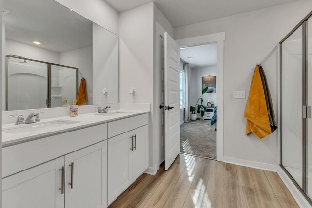 ensuite bathroom featuring double vanity, wood finished floors, a stall shower, and a sink