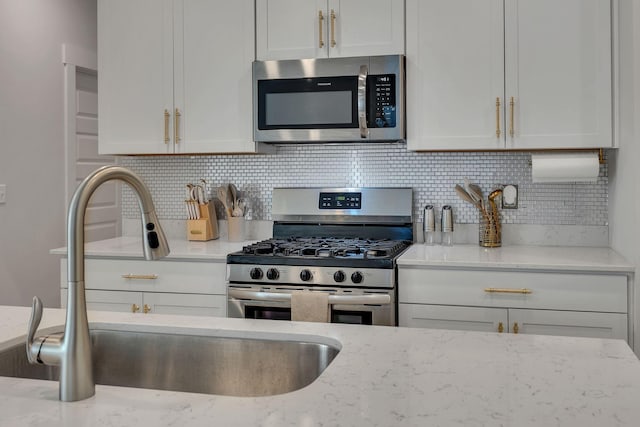 kitchen with a sink, stainless steel appliances, tasteful backsplash, and white cabinetry