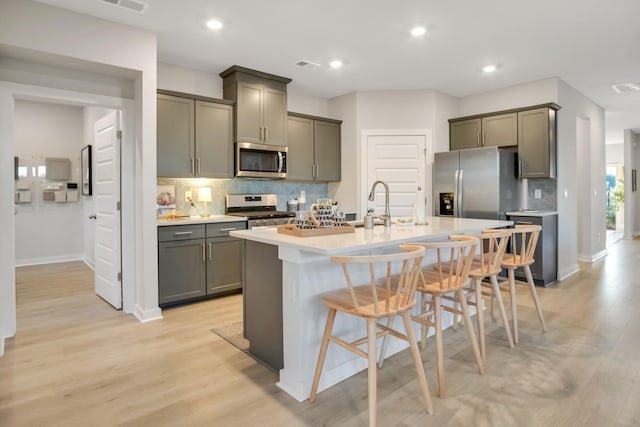 kitchen with light wood finished floors, gray cabinetry, a center island with sink, a breakfast bar, and stainless steel appliances