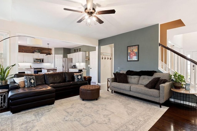 living room with stairway, wood-type flooring, and ceiling fan