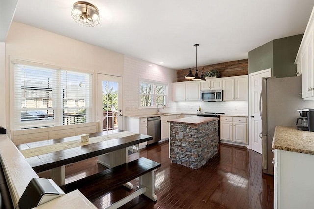 kitchen with dark wood-type flooring, a sink, a center island, stainless steel appliances, and decorative backsplash