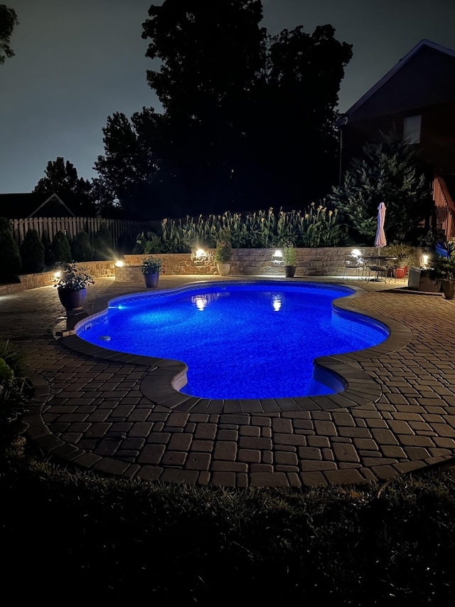 pool at twilight featuring a patio area, an outdoor pool, and a fenced backyard