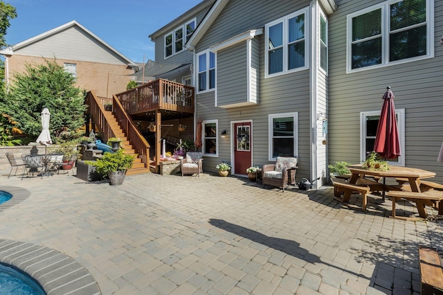 rear view of house with outdoor dining space, stairs, a patio, and a deck