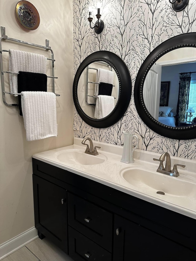 bathroom with double vanity, wallpapered walls, baseboards, and a sink