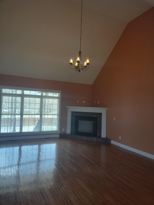 unfurnished living room with wood finished floors, baseboards, high vaulted ceiling, an inviting chandelier, and a fireplace