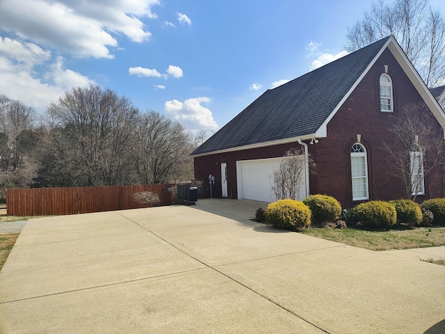 view of property exterior featuring brick siding, fence, concrete driveway, roof with shingles, and an attached garage