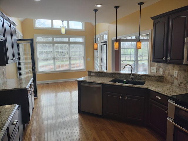 kitchen with light stone countertops, a peninsula, a sink, stainless steel appliances, and backsplash