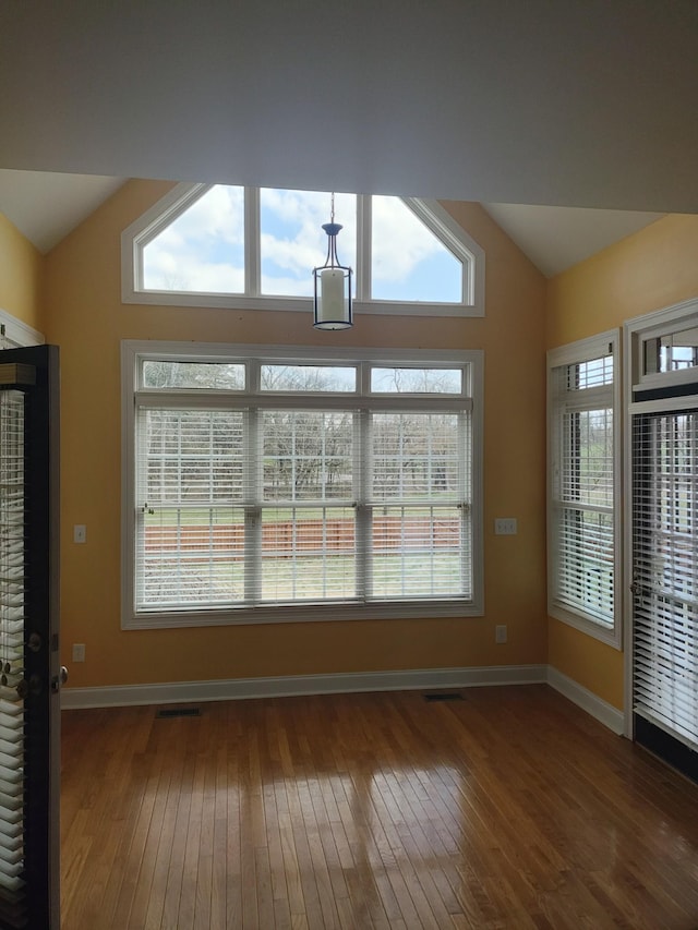 interior space with visible vents, wood-type flooring, baseboards, and vaulted ceiling