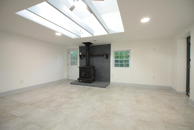 unfurnished living room with recessed lighting, a skylight, a wood stove, and baseboards