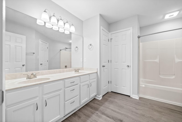 bathroom featuring double vanity, wood finished floors, shower / bathtub combination, and a sink