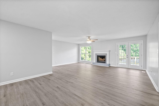 unfurnished living room with a brick fireplace, baseboards, ceiling fan, and wood finished floors