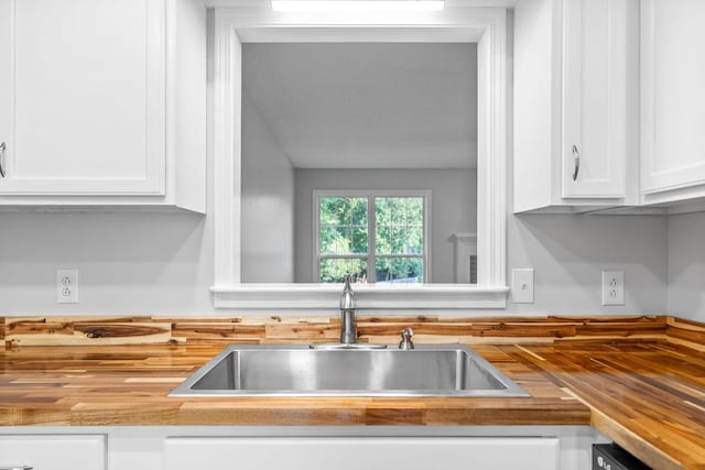 kitchen featuring a sink, dishwashing machine, butcher block countertops, and white cabinets