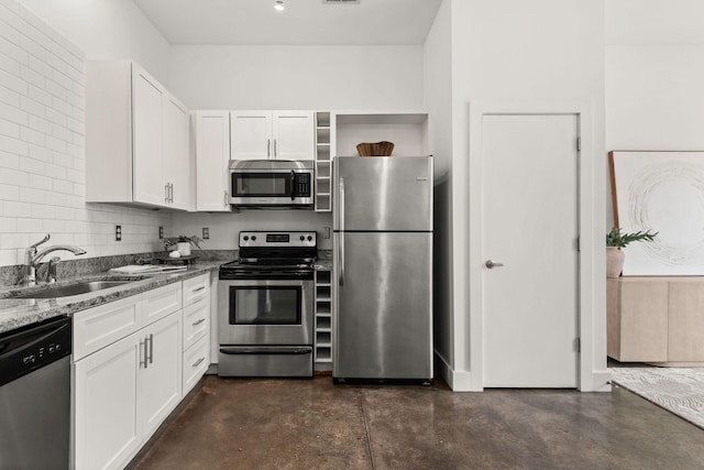 kitchen featuring light stone counters, finished concrete floors, a sink, appliances with stainless steel finishes, and white cabinetry