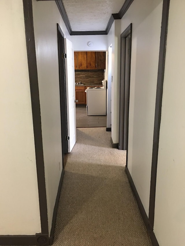 hall with baseboards, carpet, ornamental molding, a textured ceiling, and a sink