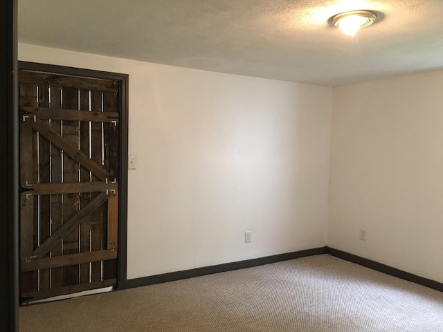 carpeted empty room featuring a textured ceiling and baseboards