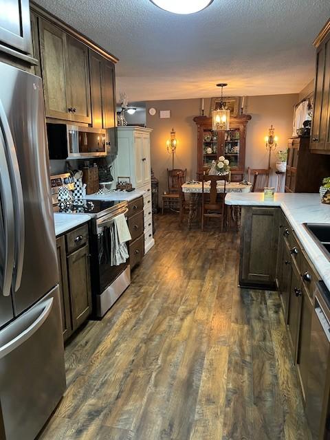 kitchen featuring a textured ceiling, appliances with stainless steel finishes, a peninsula, light countertops, and dark wood-style flooring