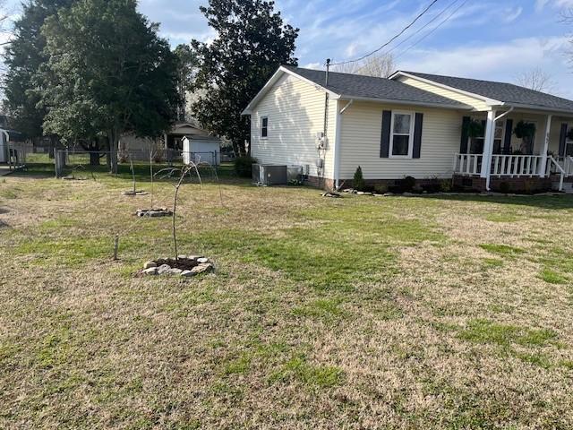 view of side of home with a yard, central AC unit, and covered porch