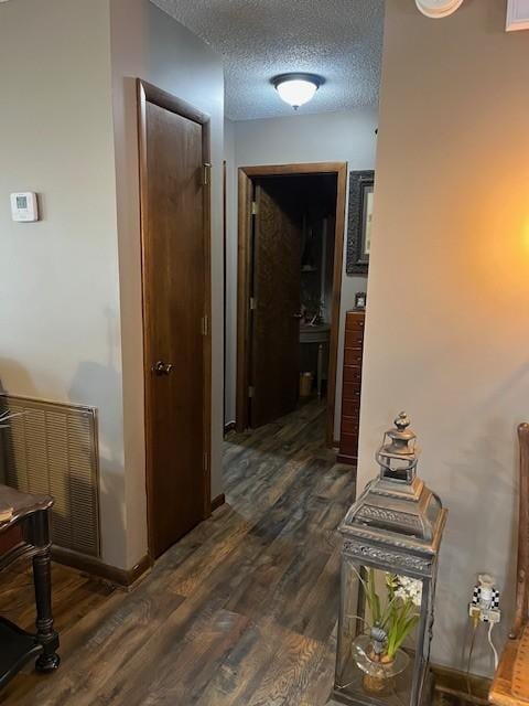 corridor with baseboards, dark wood-style floors, visible vents, and a textured ceiling