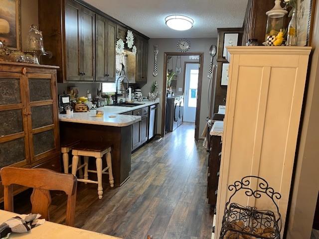 kitchen featuring a sink, dishwasher, light countertops, a peninsula, and dark wood-style flooring