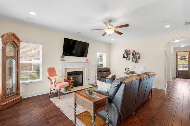 living room with dark wood-style floors, arched walkways, a high end fireplace, ceiling fan, and crown molding