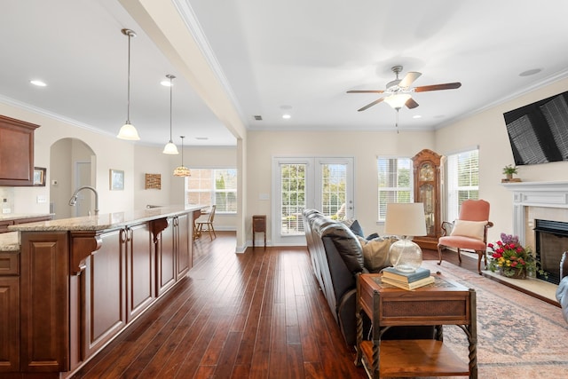 living area featuring dark wood finished floors, ornamental molding, a fireplace, arched walkways, and a ceiling fan