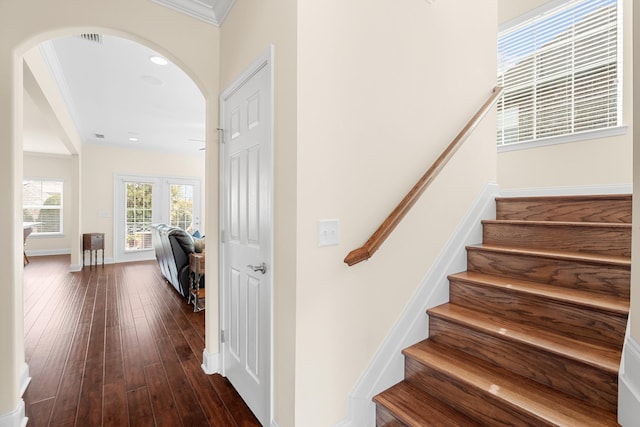 staircase featuring visible vents, hardwood / wood-style floors, arched walkways, crown molding, and baseboards