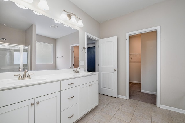 bathroom featuring double vanity, a stall shower, a walk in closet, and a sink