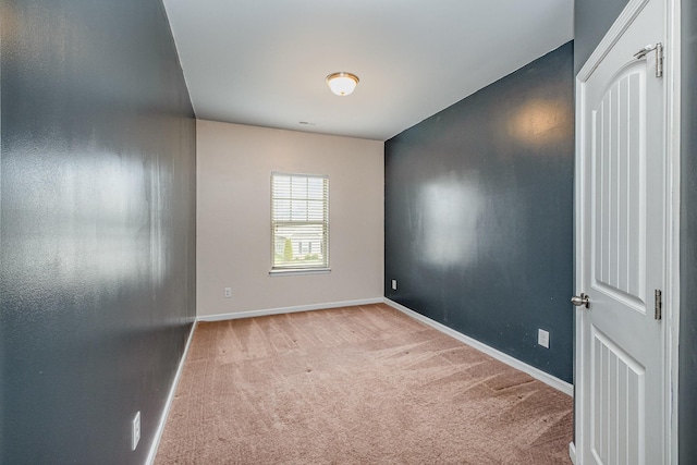 spare room featuring light colored carpet and baseboards