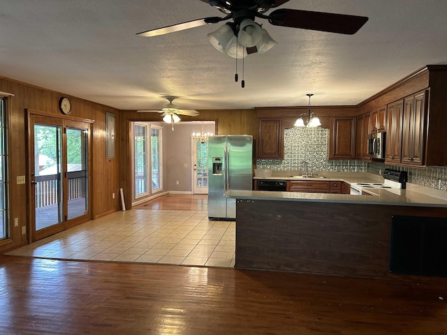 kitchen with a peninsula, a sink, stainless steel appliances, ceiling fan with notable chandelier, and light wood-type flooring