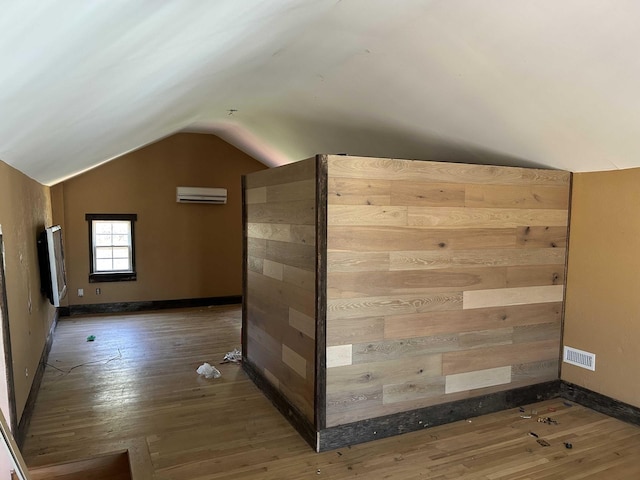 bonus room featuring vaulted ceiling, hardwood / wood-style flooring, visible vents, and a wall mounted air conditioner