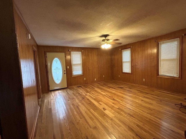 entrance foyer featuring a textured ceiling, light wood-style floors, wood walls, and ceiling fan