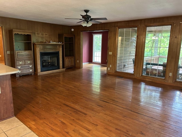 unfurnished living room featuring wooden walls, a glass covered fireplace, a ceiling fan, and hardwood / wood-style flooring