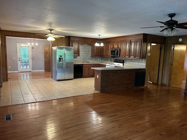 kitchen featuring visible vents, light wood-style flooring, a peninsula, ceiling fan with notable chandelier, and stainless steel appliances