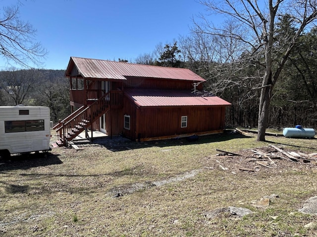 view of side of property featuring stairs, a view of trees, and metal roof