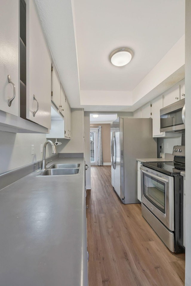 kitchen featuring a sink, stainless steel appliances, wood finished floors, and white cabinets