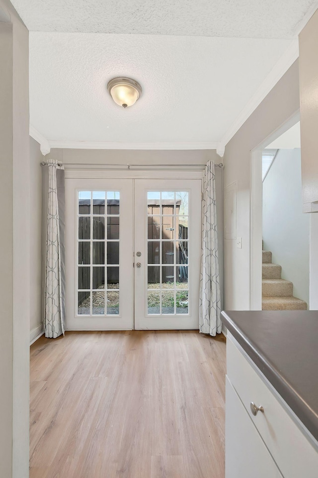 doorway with stairway, a textured ceiling, light wood-style floors, and ornamental molding