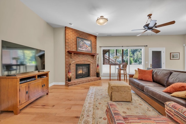 living area featuring a ceiling fan, a fireplace, baseboards, and light wood finished floors