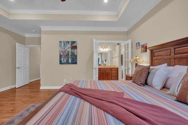 bedroom featuring wood finished floors, baseboards, a tray ceiling, ornamental molding, and connected bathroom