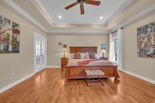 bedroom featuring baseboards, a raised ceiling, light wood-style floors, and ornamental molding