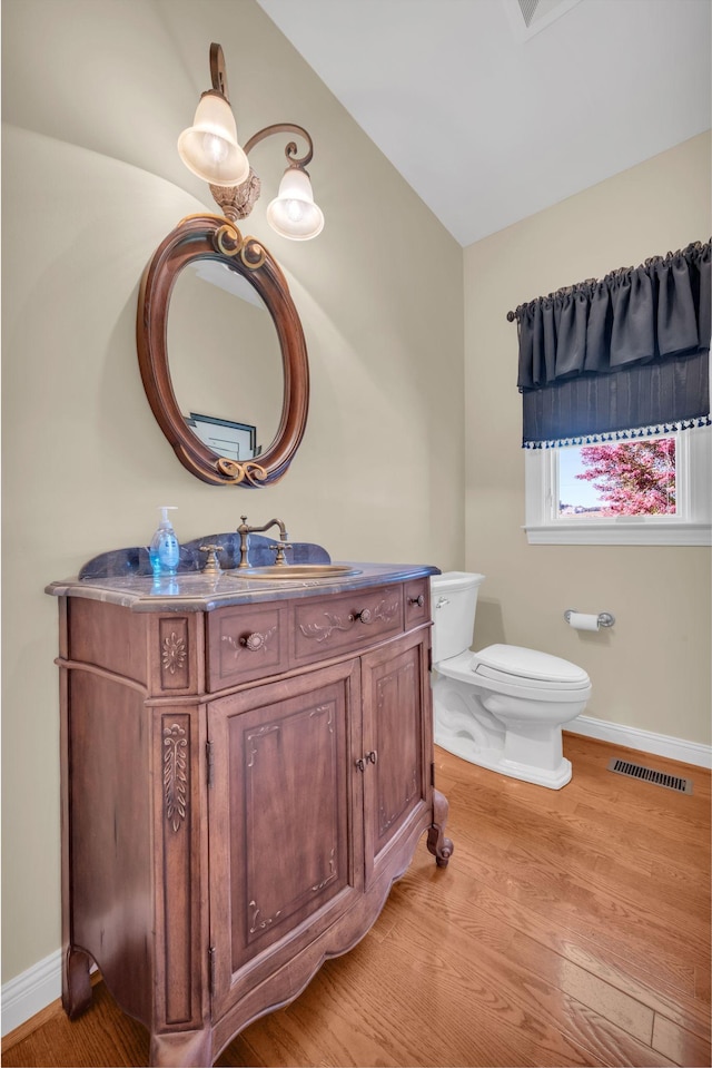 half bathroom with visible vents, toilet, wood finished floors, baseboards, and vanity