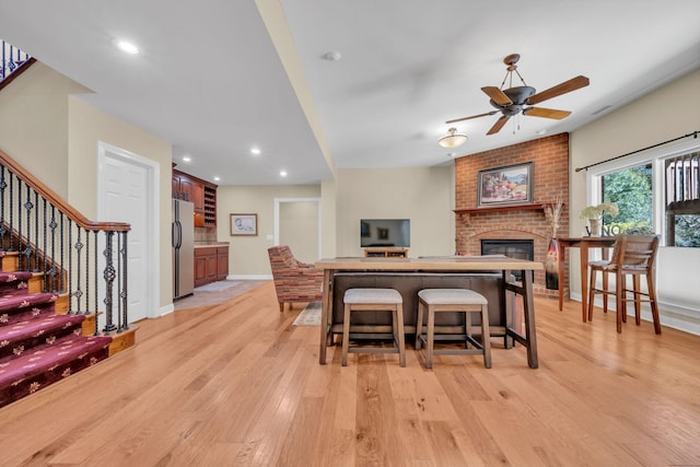 dining area featuring light wood-type flooring, a ceiling fan, recessed lighting, a fireplace, and stairs