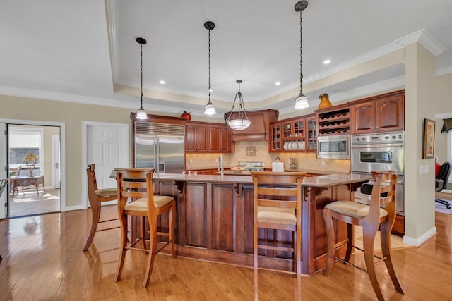 kitchen featuring a tray ceiling, backsplash, light wood finished floors, glass insert cabinets, and built in appliances