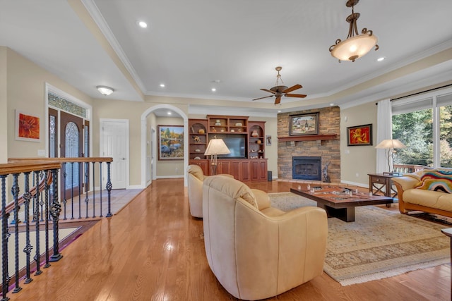 living area with light wood-style flooring, a fireplace, ceiling fan, and ornamental molding